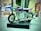 A miniature motorcycle model integrates a small clock where the engine would typically be. The model is placed on a patterned black base, and the surroundings are slightly blurred, suggesting an indoor location. Chrome elements and a transparent, dark purple piece adorn the motorcycle.