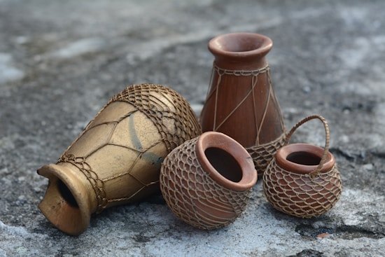 A group of earthen pots arranged on a rough, stone-like surface. The pots vary in shape and size, featuring intricate net-like patterns around them. The texture and design suggest craftsmanship and a rustic aesthetic.