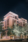 Nighttime exterior shot of a minimalist luxury apartment building illuminated with deep navy blue and olive green lighting.