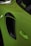 A close-up of a bright green car showing the area around the side air intake and door handle. The car's paint reflects light, and a window decal with text is visible on the edge of the window.