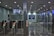 A modern subway station entrance with multiple automated gates featuring green lights. Above the gates, a surveillance camera display screen is mounted, showing live footage. The area is illuminated with ceiling lights, and there's a blue sign indicating platforms 12-13 with directional arrows in both Chinese and English.