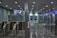 A modern subway station entrance with multiple automated gates featuring green lights. Above the gates, a surveillance camera display screen is mounted, showing live footage. The area is illuminated with ceiling lights, and there's a blue sign indicating platforms 12-13 with directional arrows in both Chinese and English.