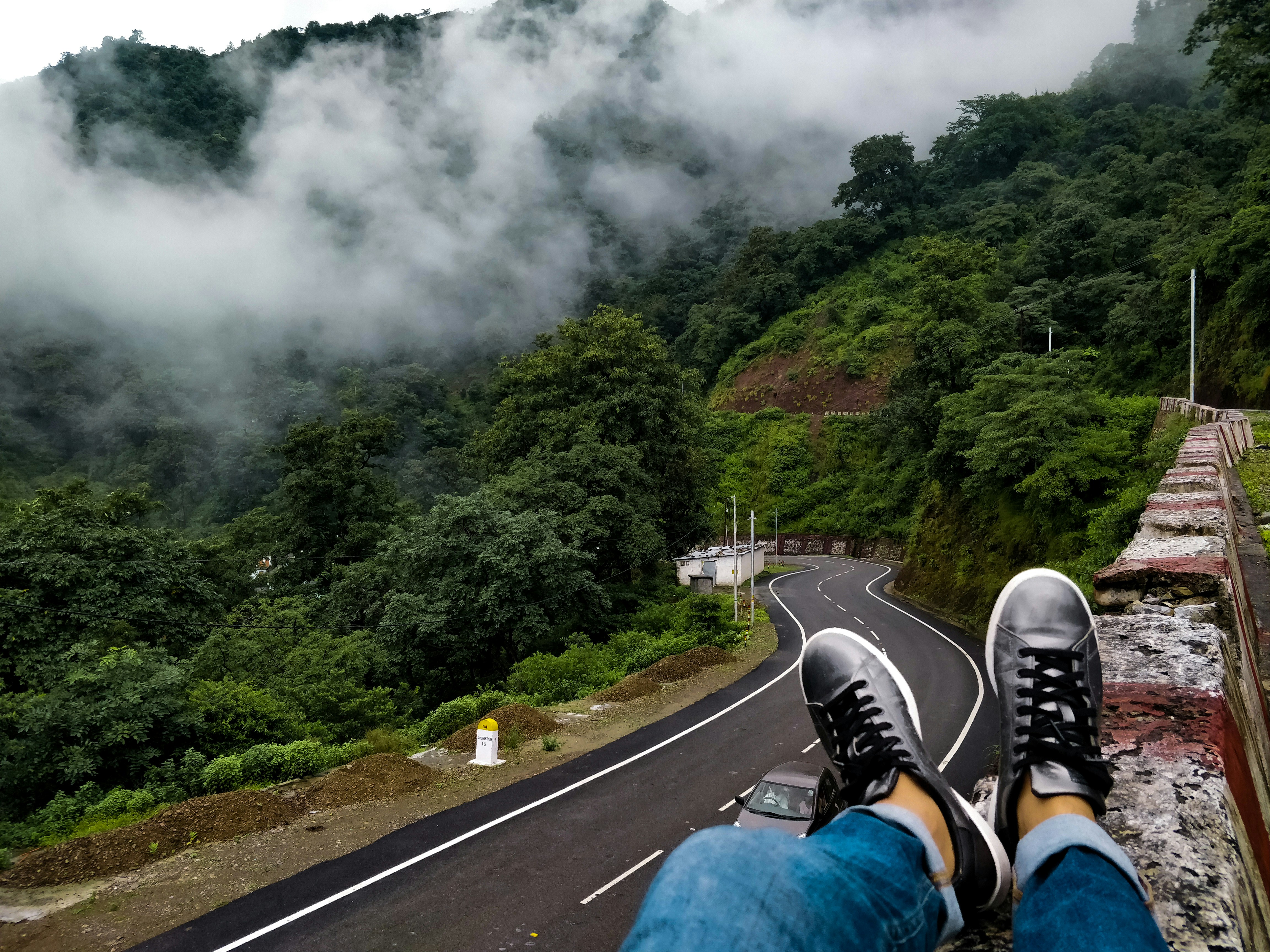 Person in blauen Jeans und schwarzen Schuhen sitzt auf Steinbarrikade