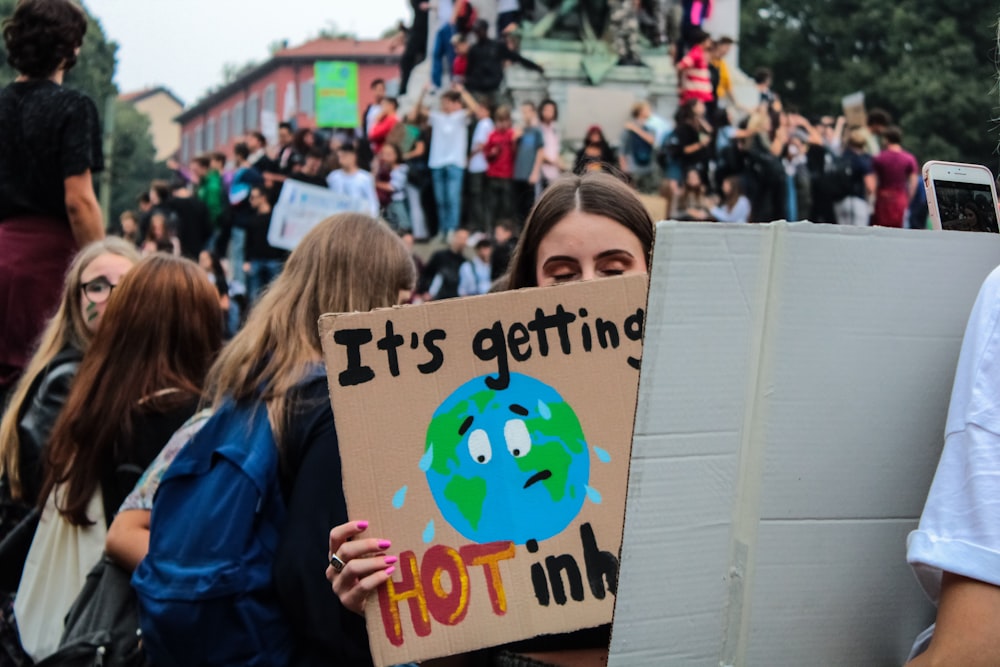 a woman holding a sign that says it's getting hot in the world