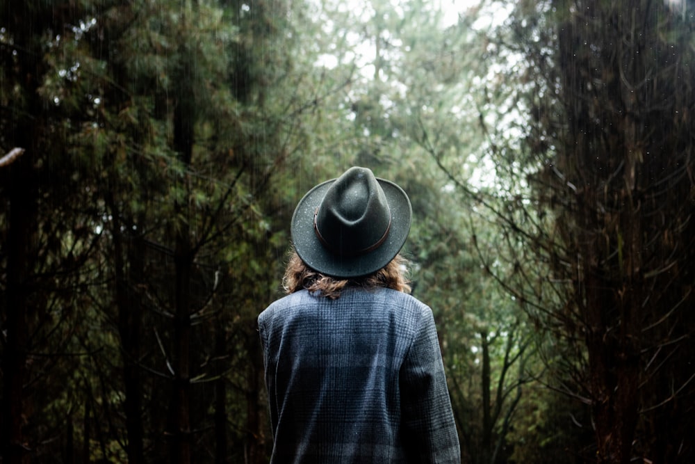 photo of person wearing gray shirt and gray fedora hat walking on forest