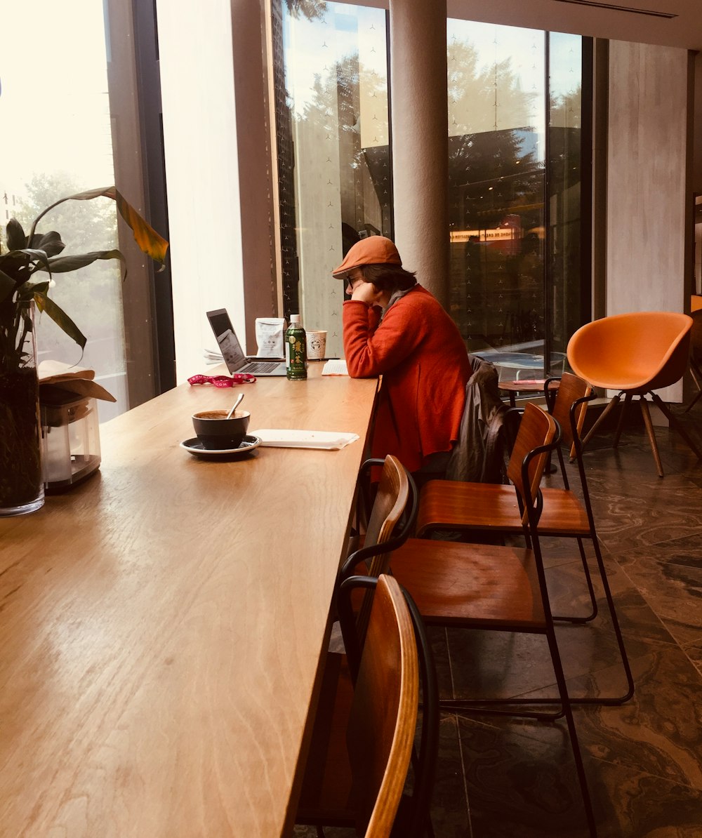 person wearing orange jacket sitting on chair while using laptop