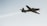 A single-engine aircraft is captured in flight against a clear sky, trailing a visible stream of white smoke. The aircraft appears to be small and possibly designed for aerobatics or training.