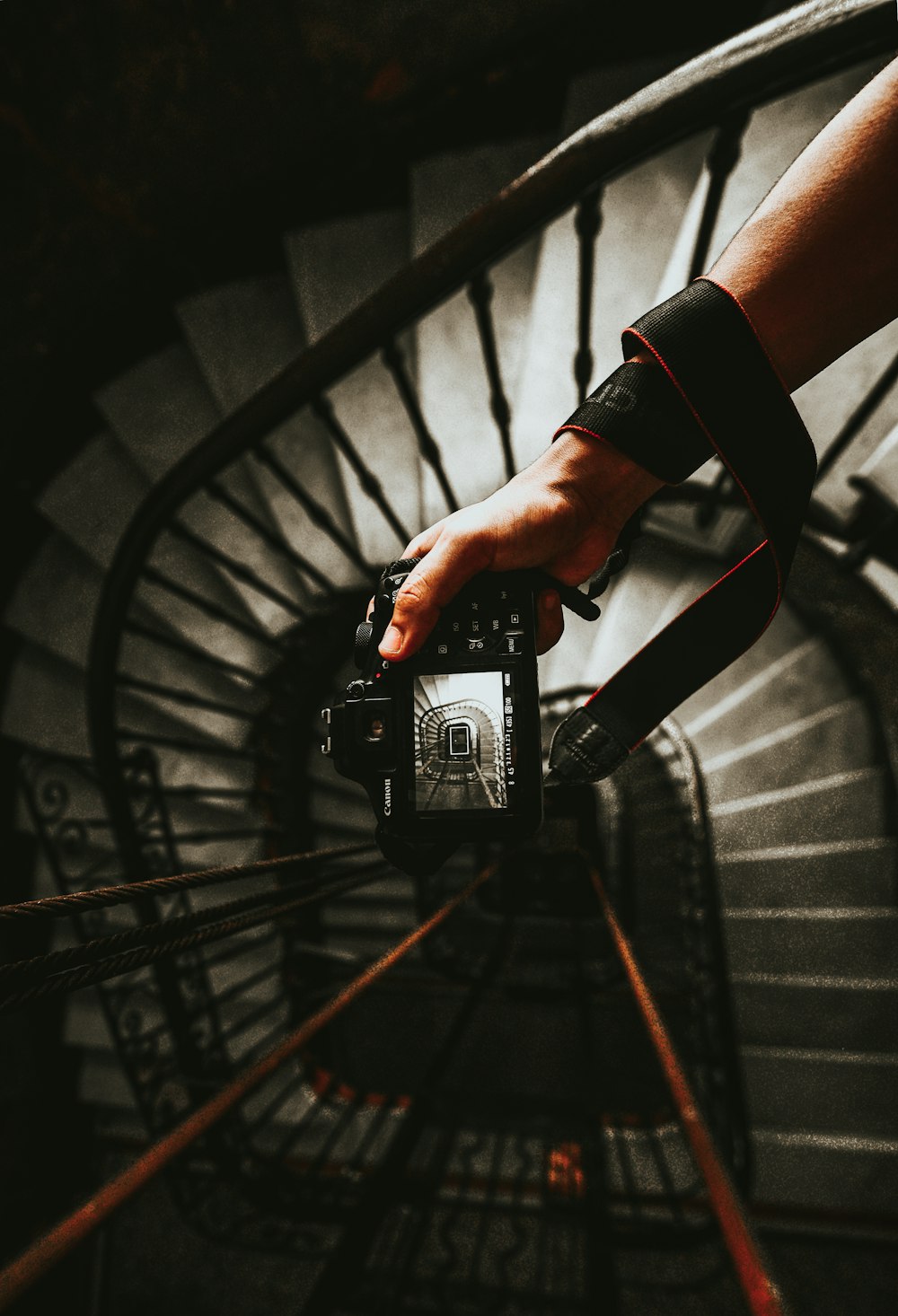 person holding black DSLR camera taking photo of spiral stairs