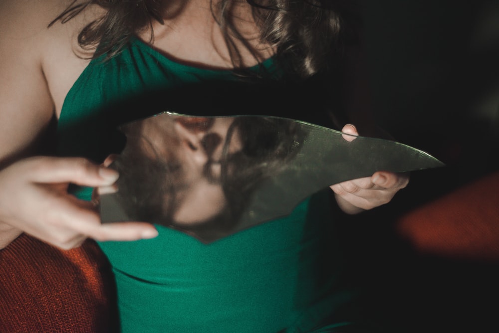 woman in green top holding glass mirror