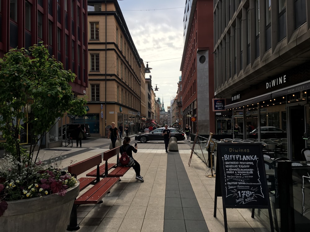 woman sitting on bench near people, buildings, and cars