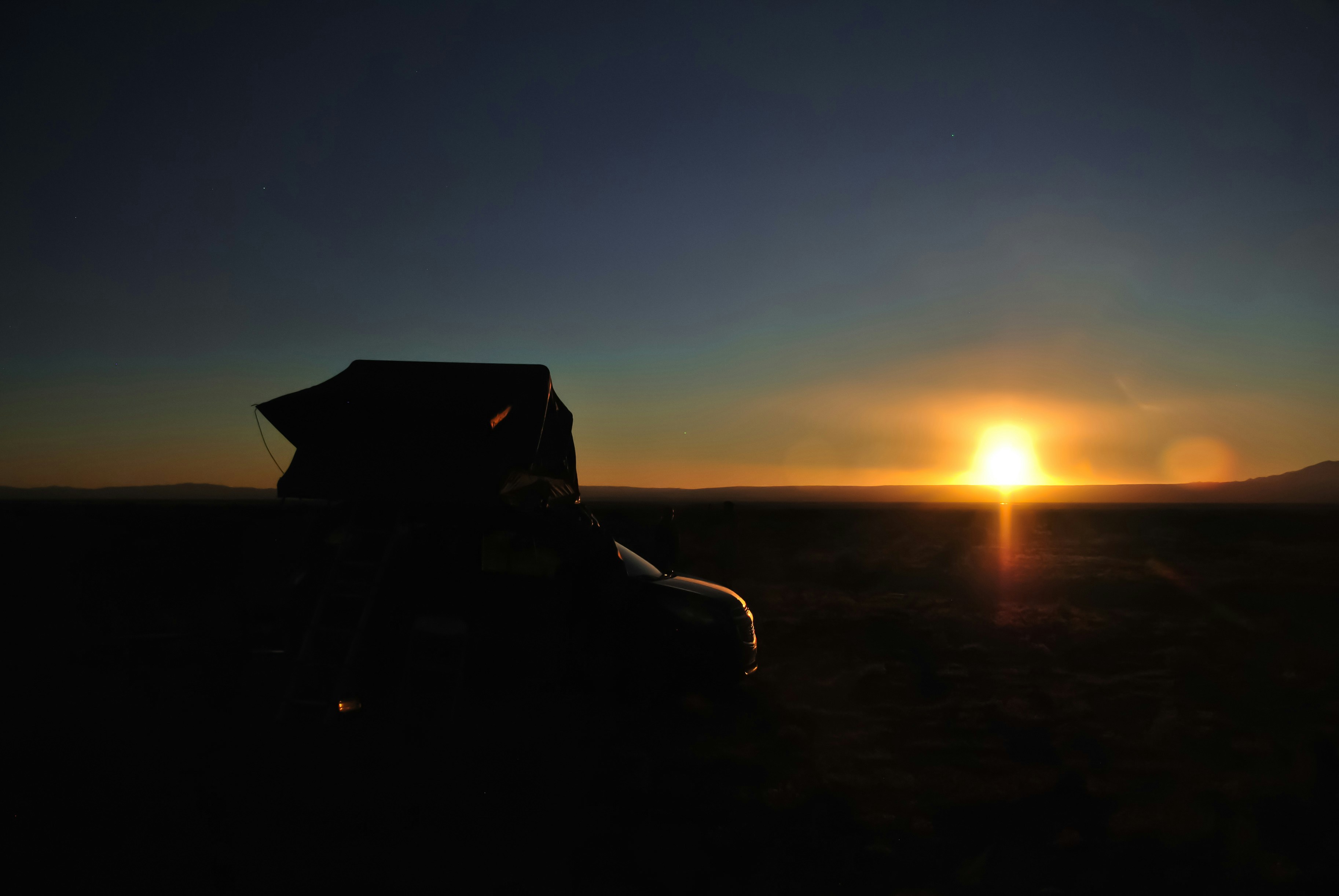 the sun is setting behind a vehicle in the desert