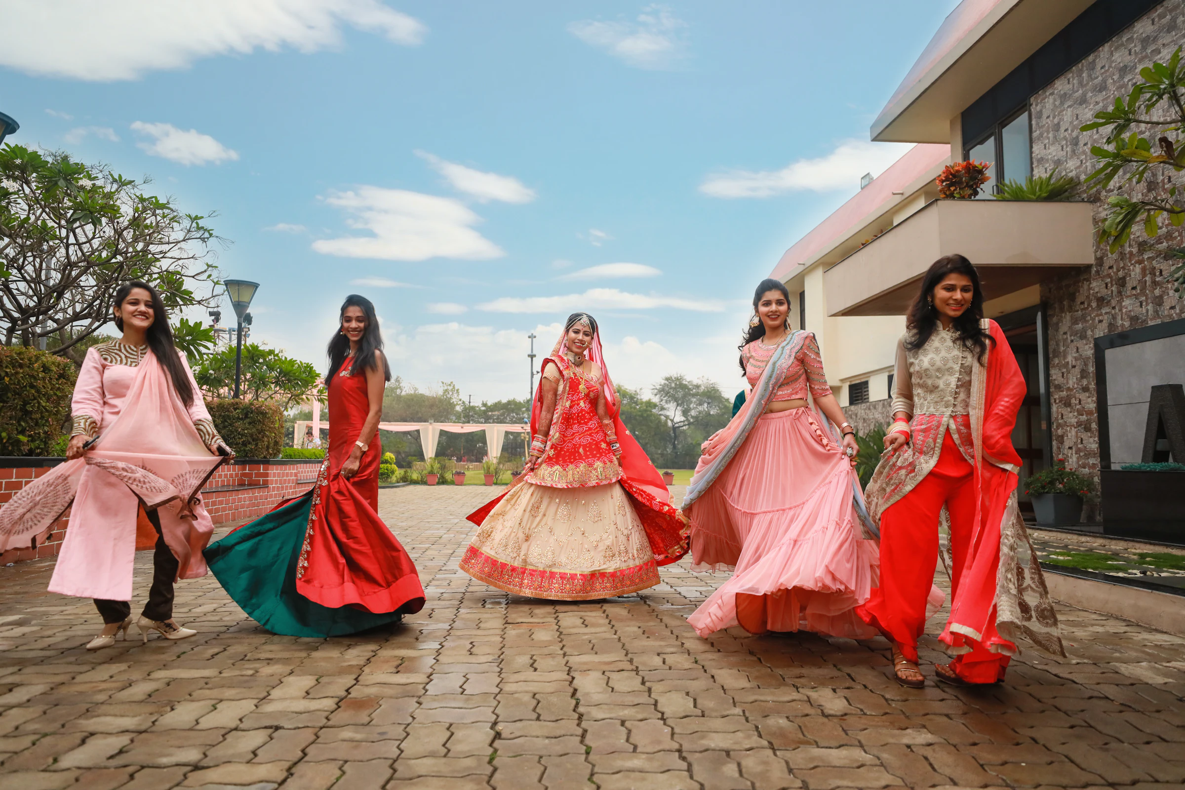 Five women in red and pink ethnic wear twirling on a sunny street