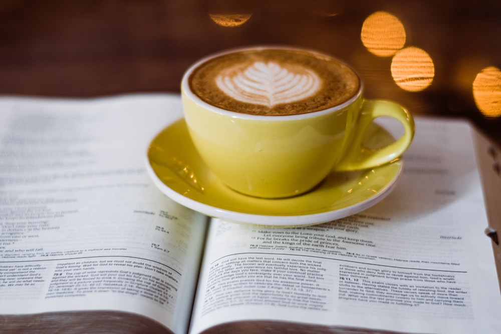 close-up photo of yellow ceramic teacup with coffee and saucer on top of book