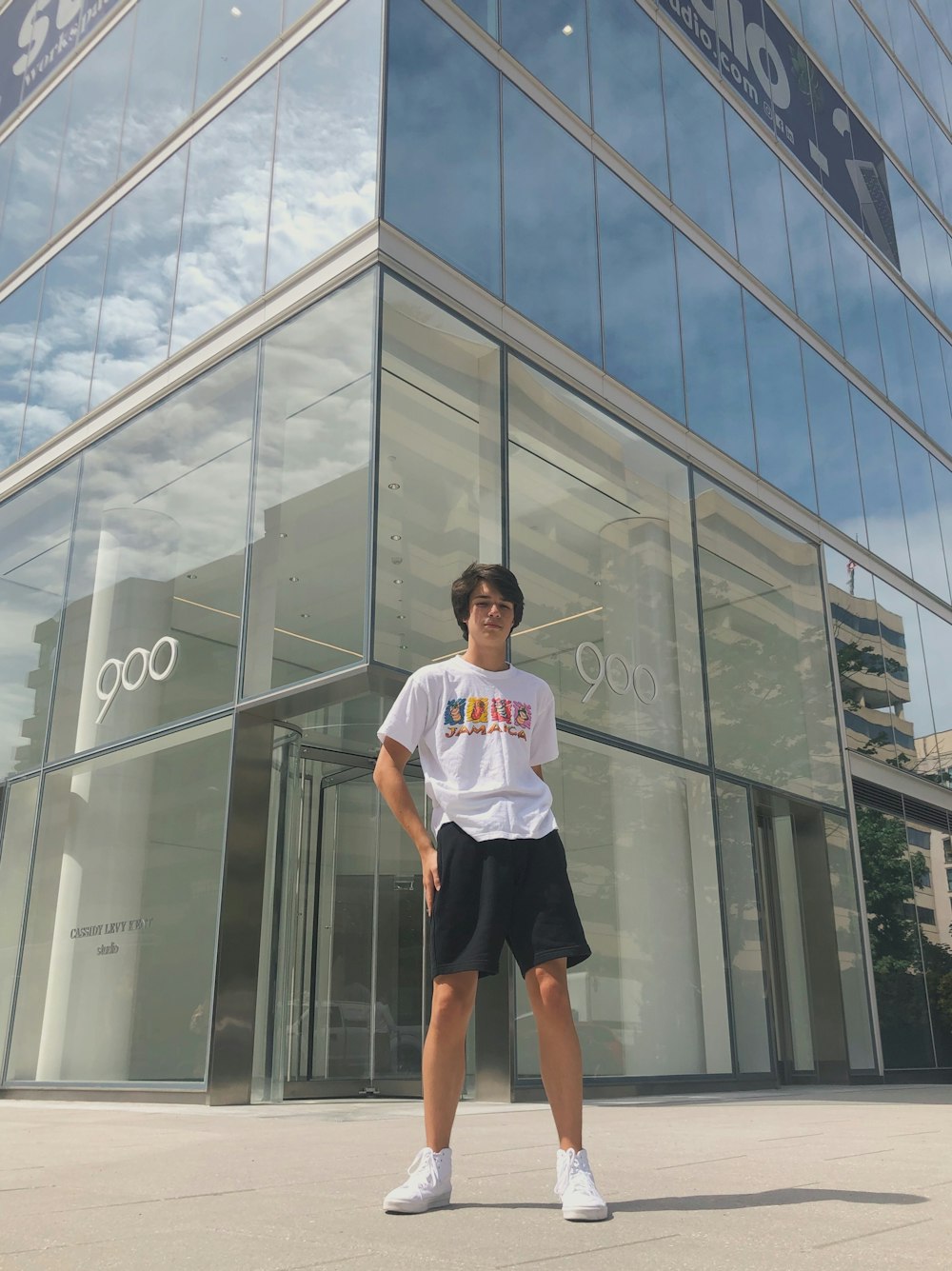 Hombre con camisa blanca de cuello redondo de pie junto a un edificio de vidrio