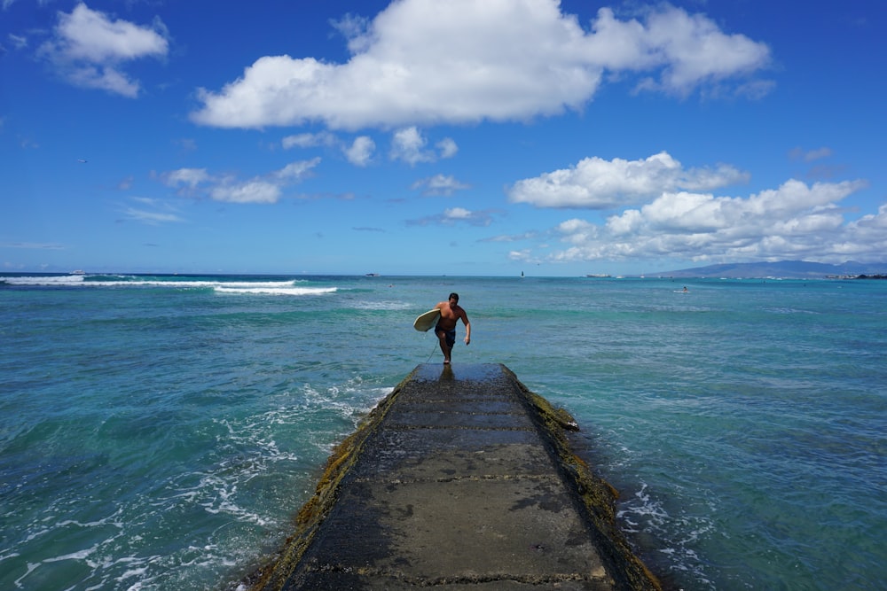 man walking on dock holding surfboard