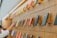 A wall display showcasing an array of colorful smartphone cases mounted on a wooden panel, arranged in a neat and orderly manner. The cases vary in colors including blue, red, and yellow. A person's hand is reaching towards one of the cases.