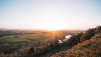 An expansive landscape with a rising sun over gentle hills.