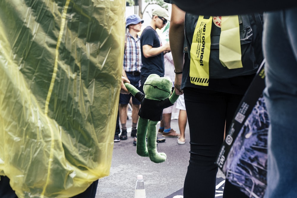 a green teddy bear sitting in the middle of a crowd