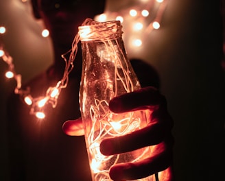 person holding bottle with string lights