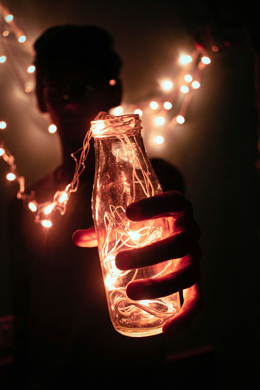 person holding bottle with string lights