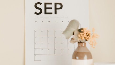 a desk with a calendar and a vase of flowers
