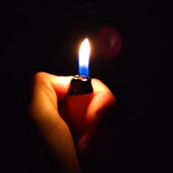 A hand holding a premium lighter with electric blue accents illuminating in low light.
