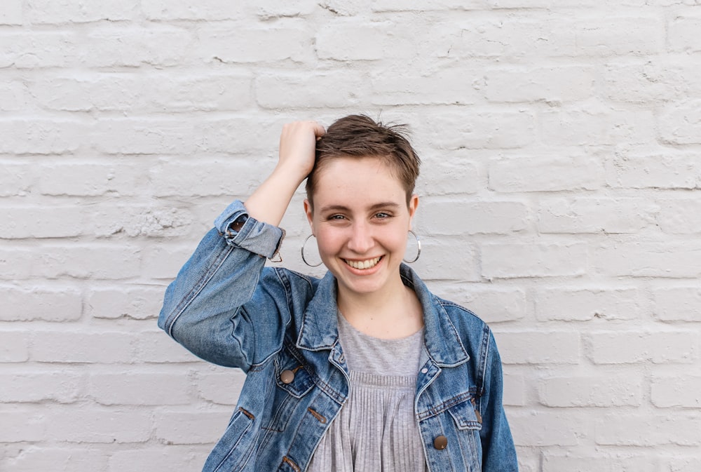 woman in blue denim jacket and gray crew-neck top holding her hair