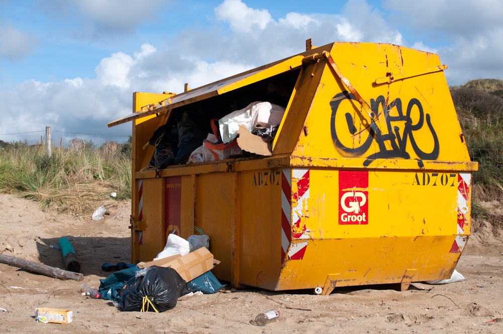 yellow garbage bin with trash on sand dunes