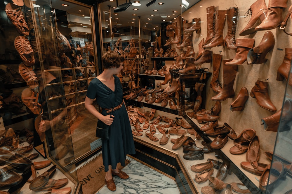 mujer con vestido negro de pie frente a zapatos de cuero marrón