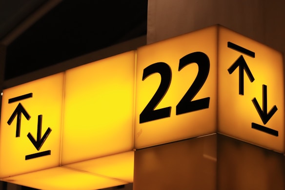 A bright, illuminated yellow sign with the number 22 prominently displayed, accompanied by upward and downward arrow symbols. The sign appears to be located indoors, possibly indicating directions or levels.