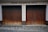 Two adjacent wooden garage doors with a weathered and worn appearance, set in a stone and concrete facade. Above the doors, the words 'FREIW. FEUERWEHR SPITZ' are displayed in bold, dark lettering. The ground is covered in cobblestones.