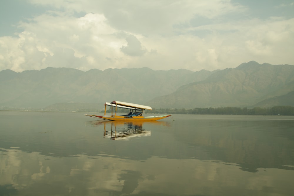 yellow boat on body of water viewing mountain under white and gray skies during daytime