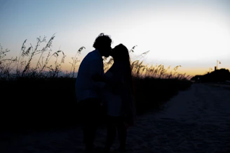 Sunlit couple sharing a quiet moment outdoors, with warm sand tones in the background.