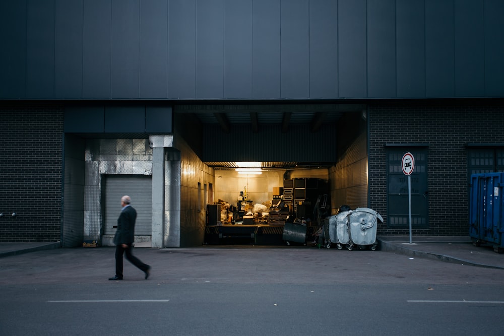 man wearing black suit walking on pathway near building showing lights on