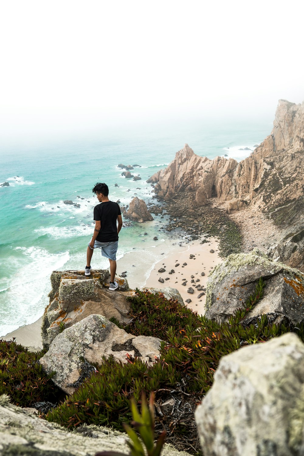 man standing on cliff near body of water