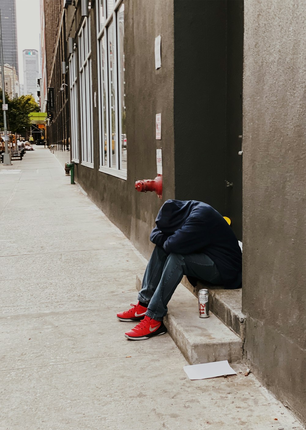 person wearing blue hooded jacket sitting while hiding face on concrete pathway