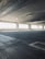 An empty parking garage with concrete floors and ceilings, featuring large windows that allow natural light to filter in. The structure is characterized by its industrial aesthetic, with visible steel beams and reinforced concrete.