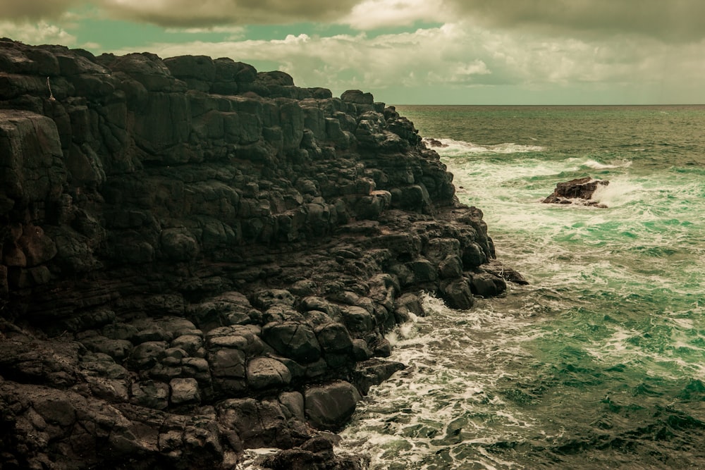 waves crashing on cliff under cloudy sky during daytime