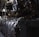 A complex array of industrial machinery and pipes with a large valve wheel dominates the scene. The machinery appears metallic and rugged, with various interconnected components.