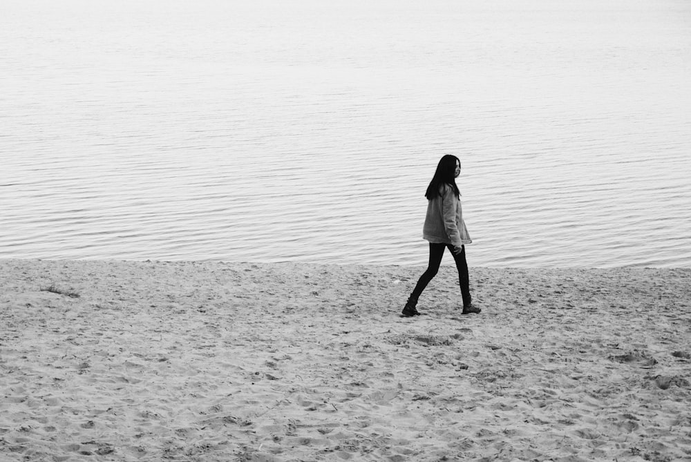 a woman walking on a beach next to a body of water