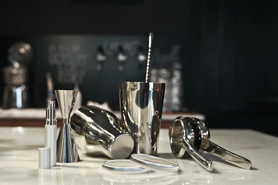 A sleek black and gold cocktail shaker surrounded by fresh ingredients and delicate glassware on a polished bar counter.