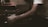 A person wearing a white shirt is engaged in a task involving a piece of paper and a pen or similar writing tool. The setting appears dimly lit, suggesting a focused or intimate atmosphere. The arm resting on a surface adds to the sense of concentration.
