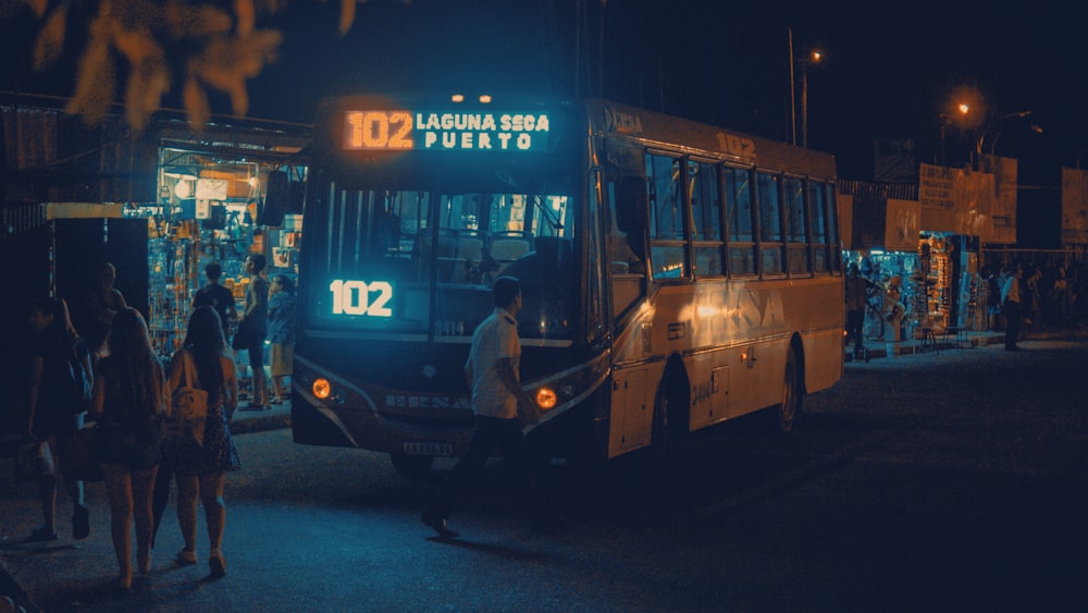 a group of people standing outside of a bus at night