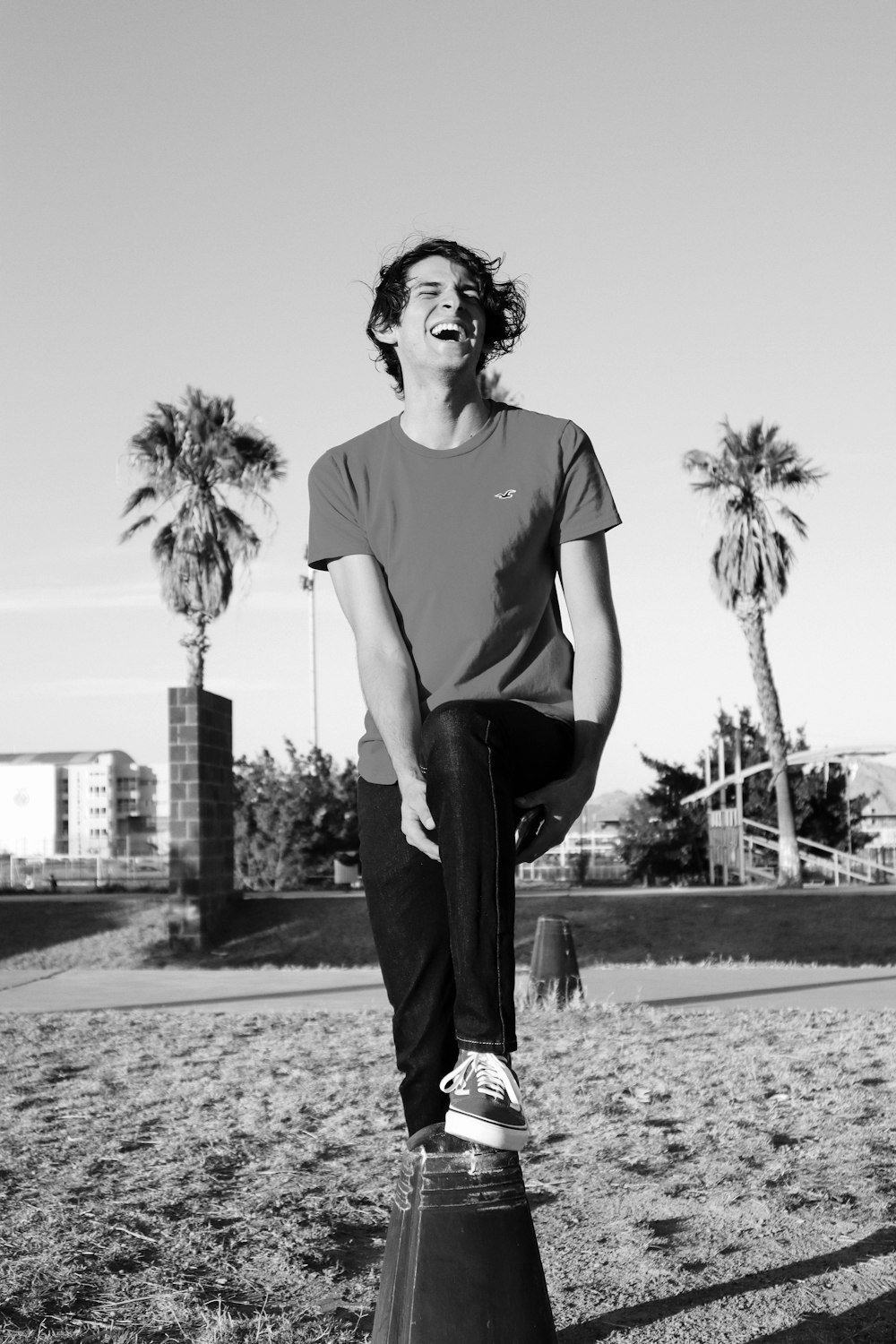 grayscale photography of man wearing crew-neck t-shirt and pants standing and laughing in field
