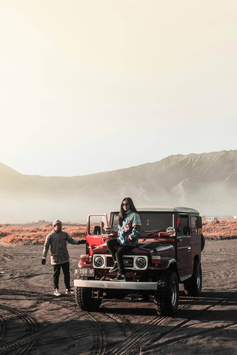 woman sitting on red vehicle near man