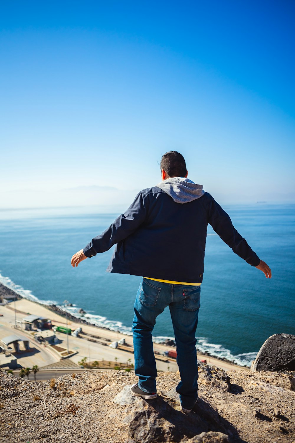 man stands on mountain near shore