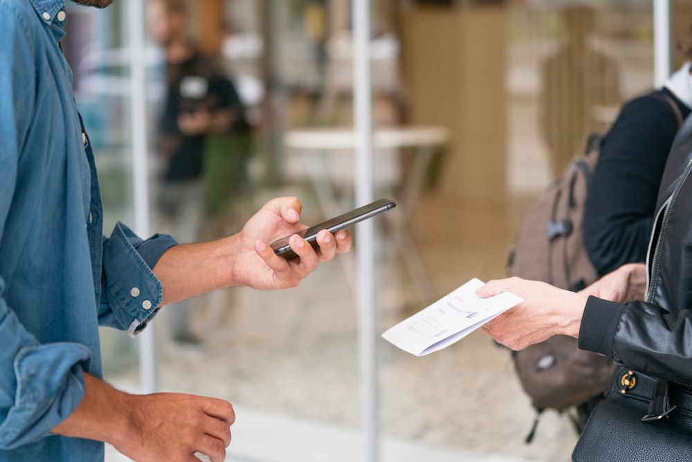 uomo che tiene lo smartphone davanti alla persona in giacca di pelle nera