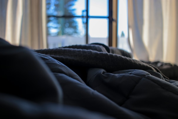 A peaceful bedroom with layered bedding and gentle natural light filtering through curtains.