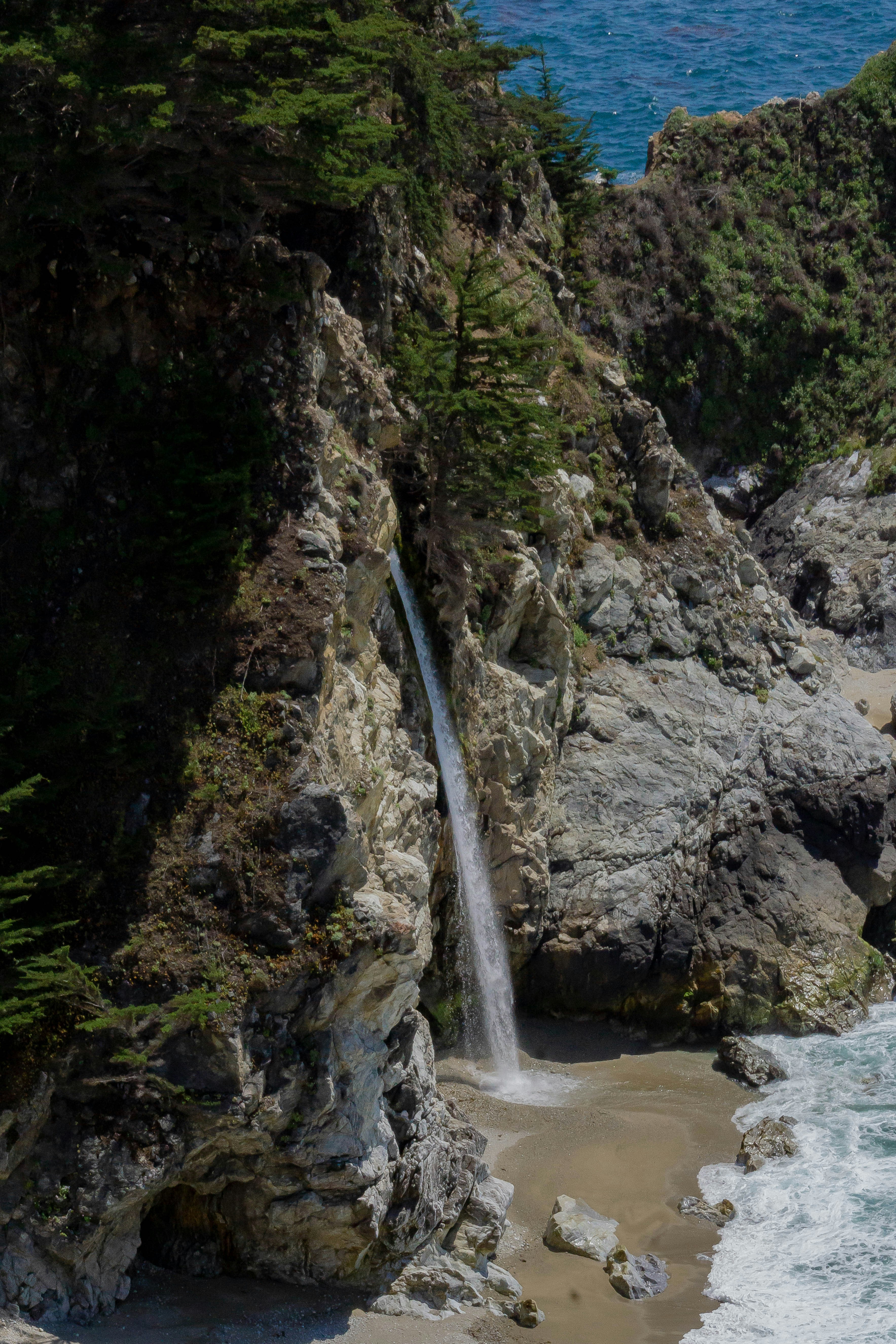 waterfalls near rock formations viewing body of water during daytime