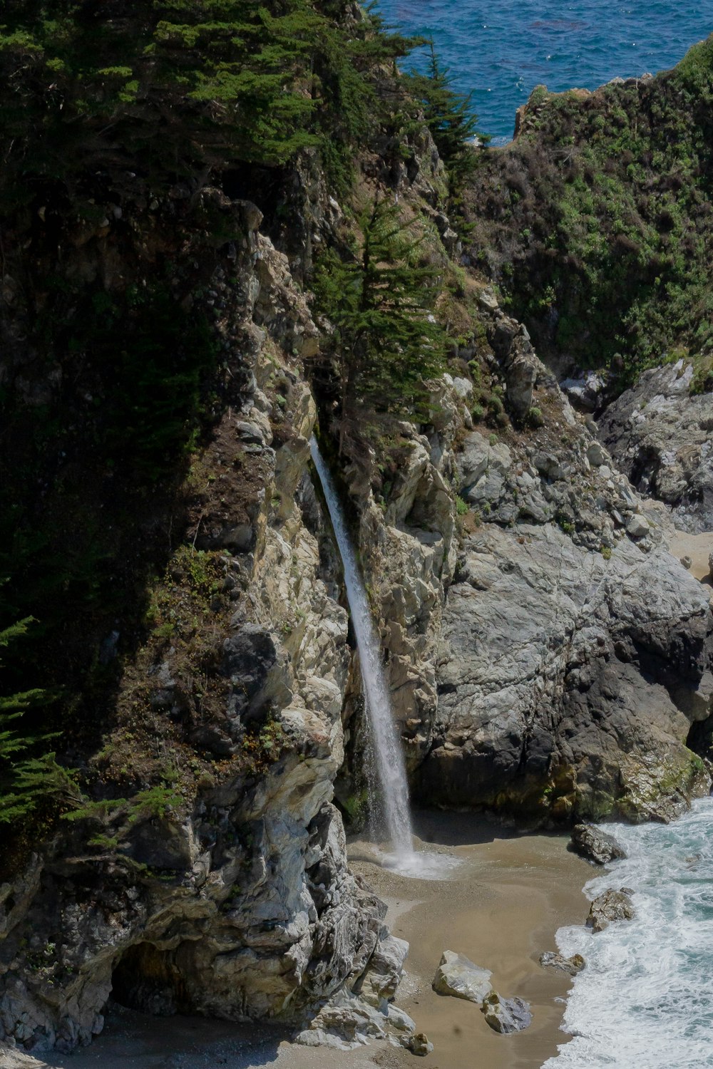 waterfalls near rock formations viewing body of water during daytime